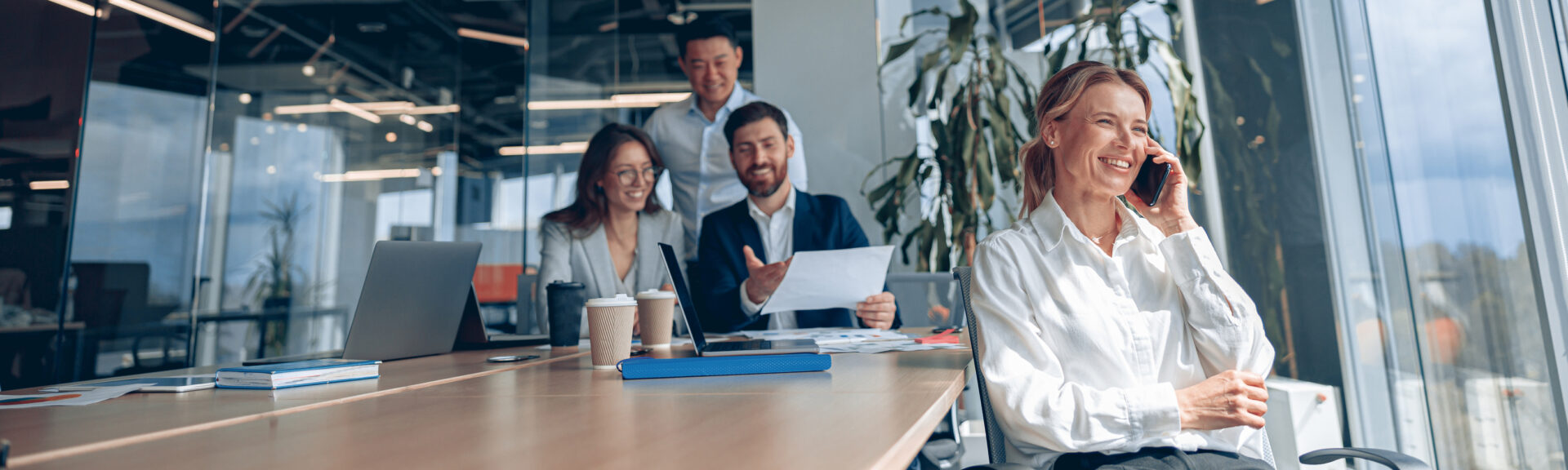 Smiling mature businesswoman is sitting on a chair and talking on phone during meeting in office