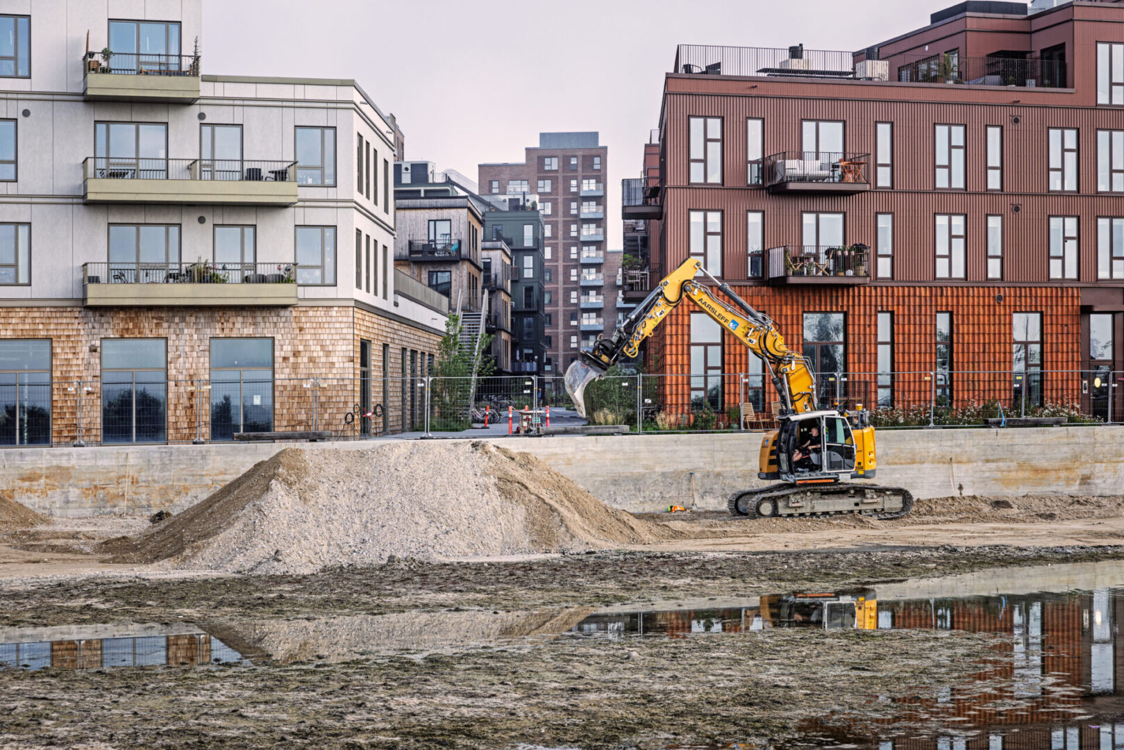 Ørestad, Copenhagen, Denmark - July 15th 2025:  A big digger is deepening an artificial lake in front of a modern housing development. The photo was taken in southern Ørestad, a newly built suburb of Copenhagen just twenty minutes from City Hall Square.